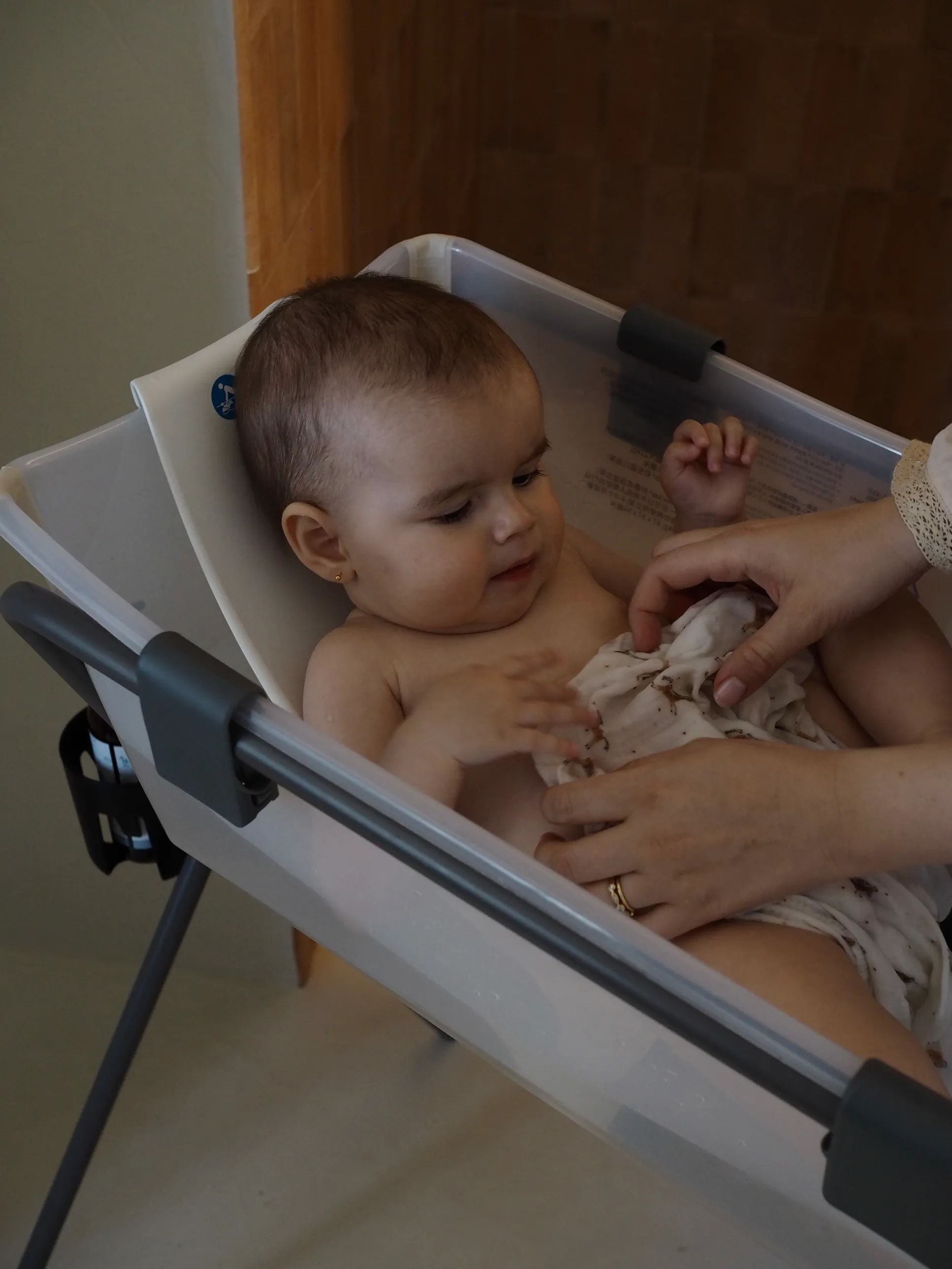A lifestyle shot of a parent bathing a toddler in a white baby bath seat on a warm home background.