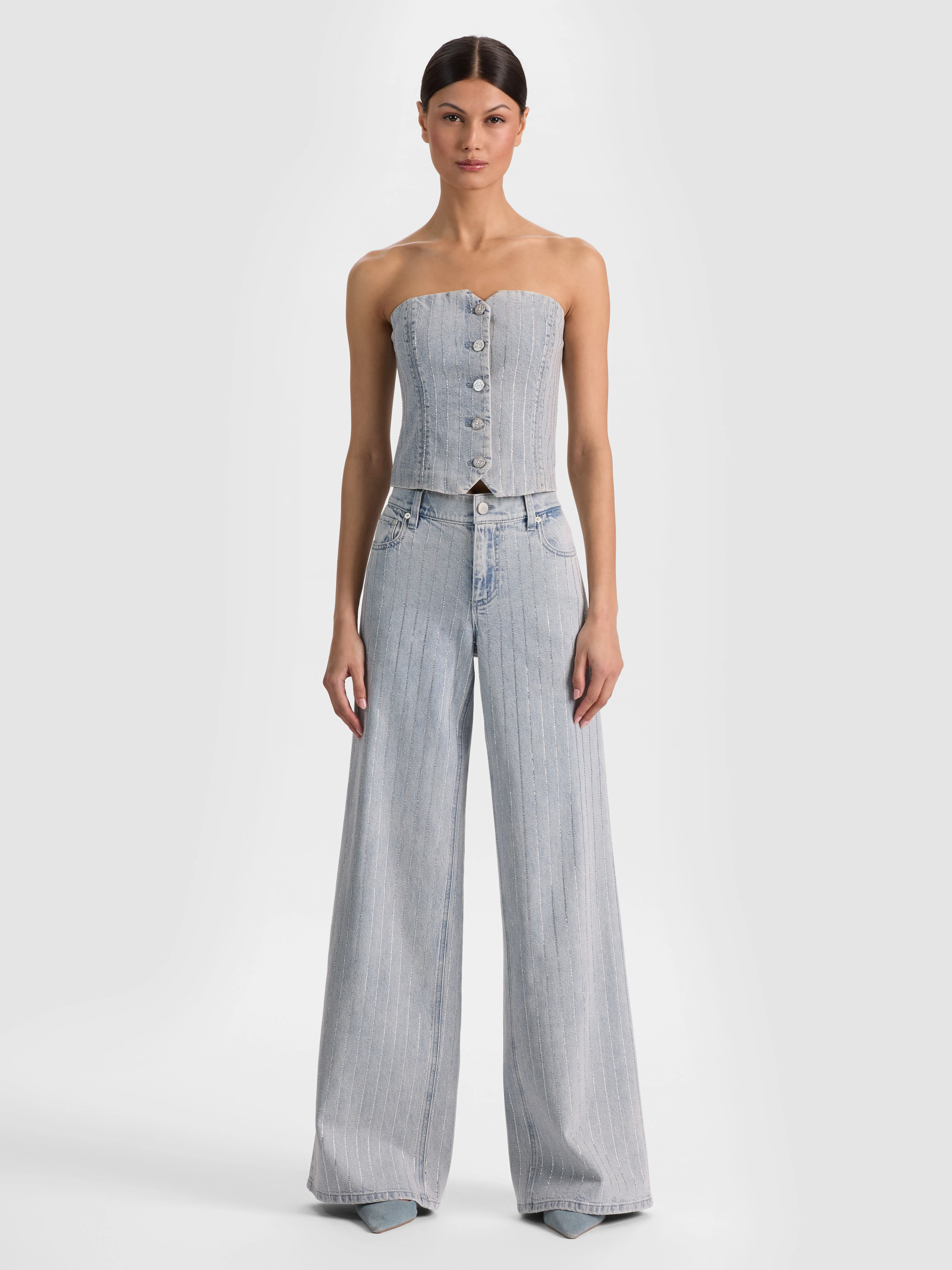A full-body head-to-toe shot of a model wearing the ALICE + OLIVIA Amazing Embellished Jean in Rockstar Blue with a tucked-in tee and belt, showcasing an elevated everyday casual outfit.