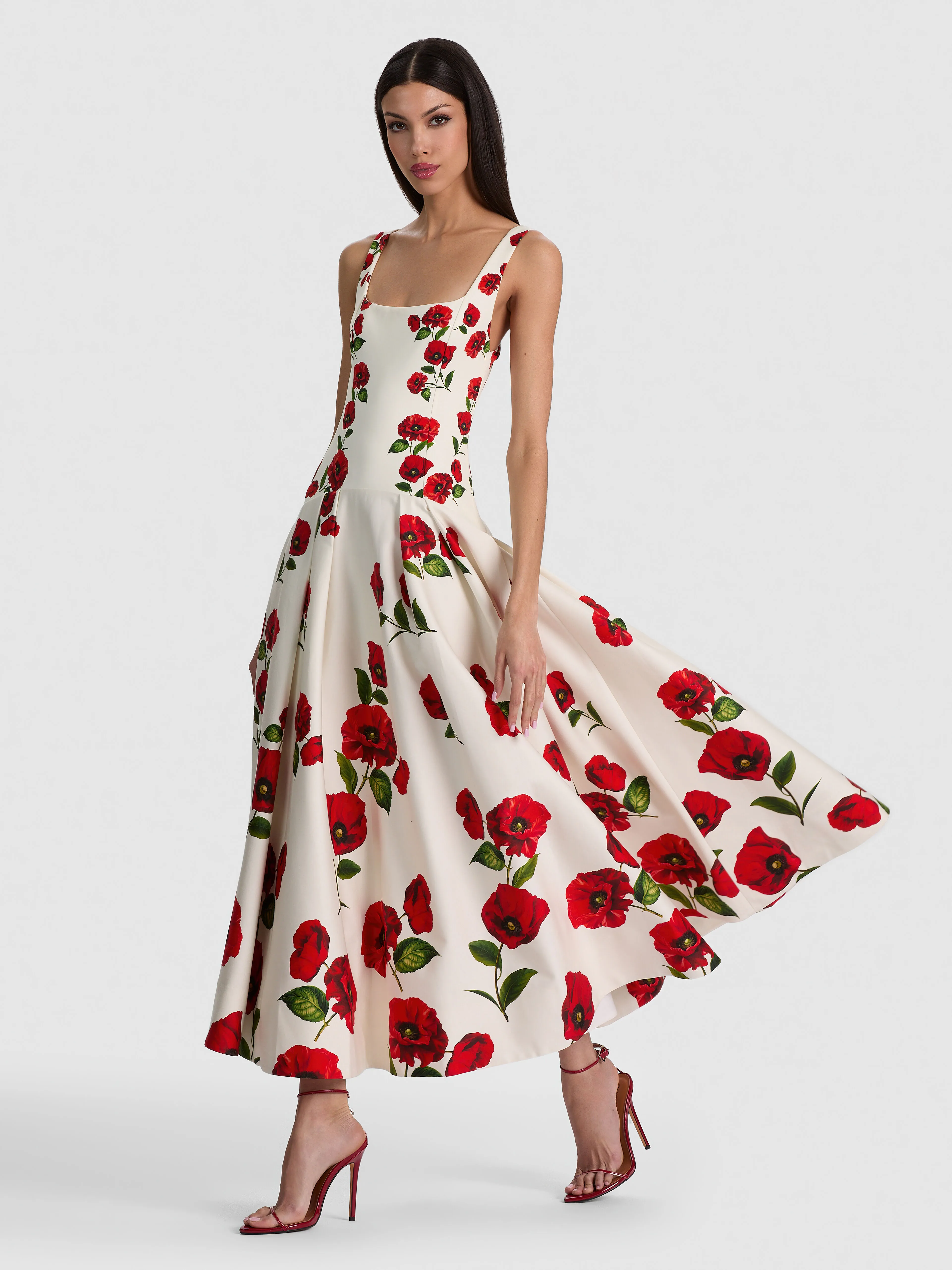 A lifestyle image of a woman wearing the ADLEY DROP WAIST DRESS with a softly pleated skirt in printed cotton sateen, styled with heels and understated accessories for an elevated daytime event.