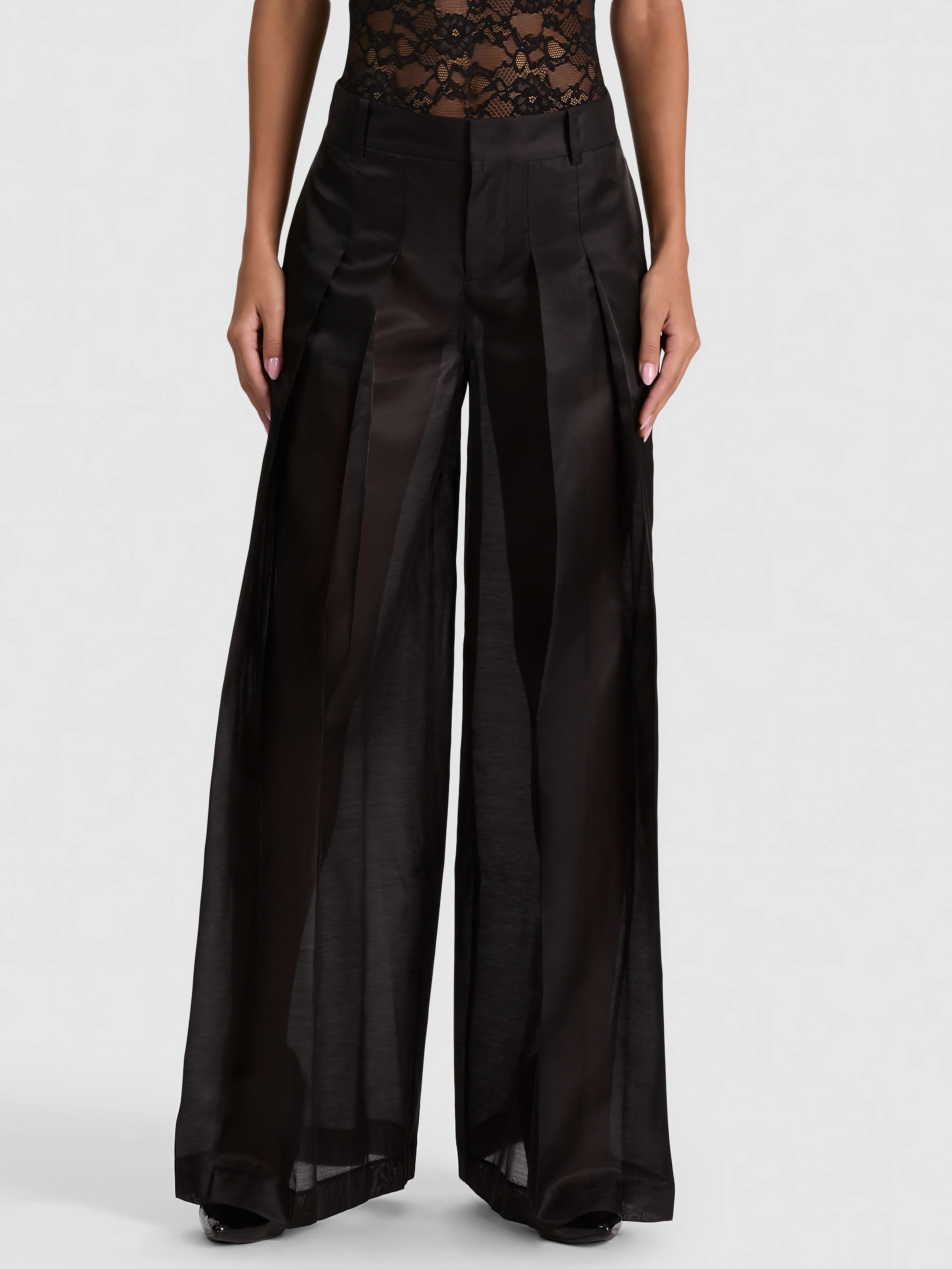 A model wearing the ALICE + OLIVIA Blaire Pleated Sheer Pant styled as an occasion suit look with a tailored blazer and heels, photographed for an elegant evening event setting.