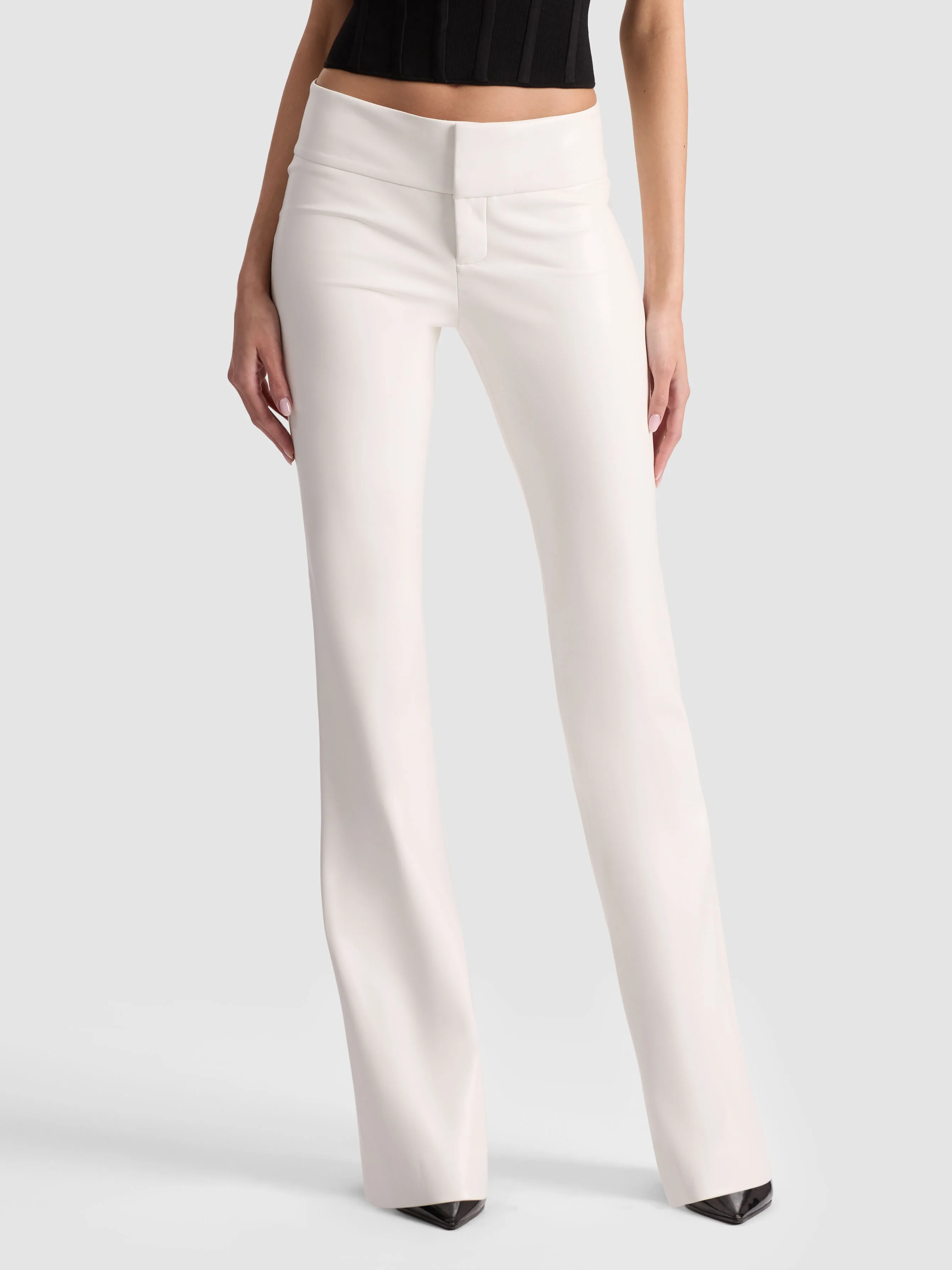 A glamorous editorial of the ALICE + OLIVIA Olivia Vegan Bootcut Pant in off-white vegan leather, styled with a sleek top and heels against a moody dark backdrop — bright, bold, and unexpected.