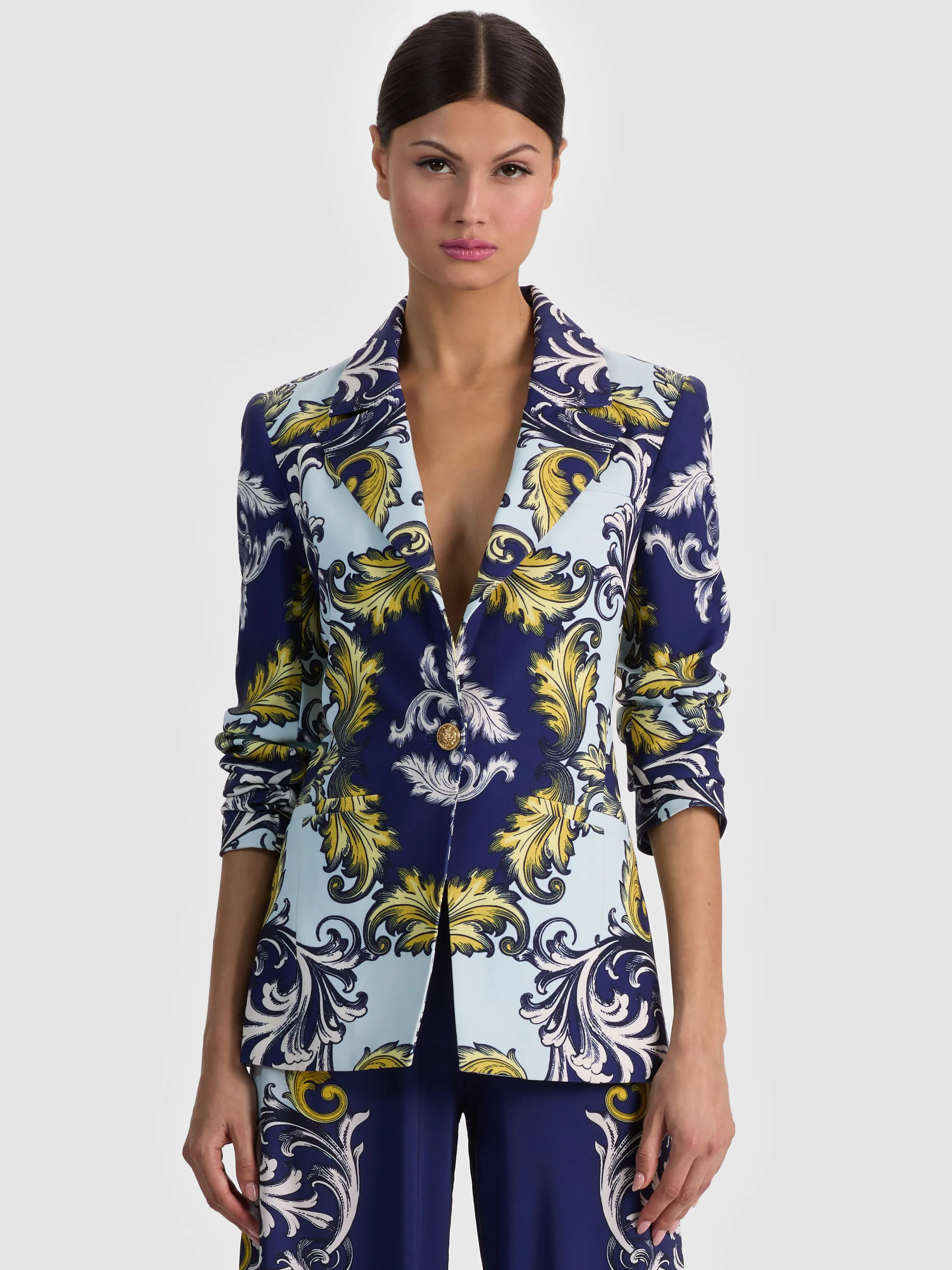 A model wearing the ALICE + OLIVIA Hope Fitted Blazer in a printed matte satin crepe, styled in a polished yet relaxed dressy casual outfit, shot in an editorial fashion setting.