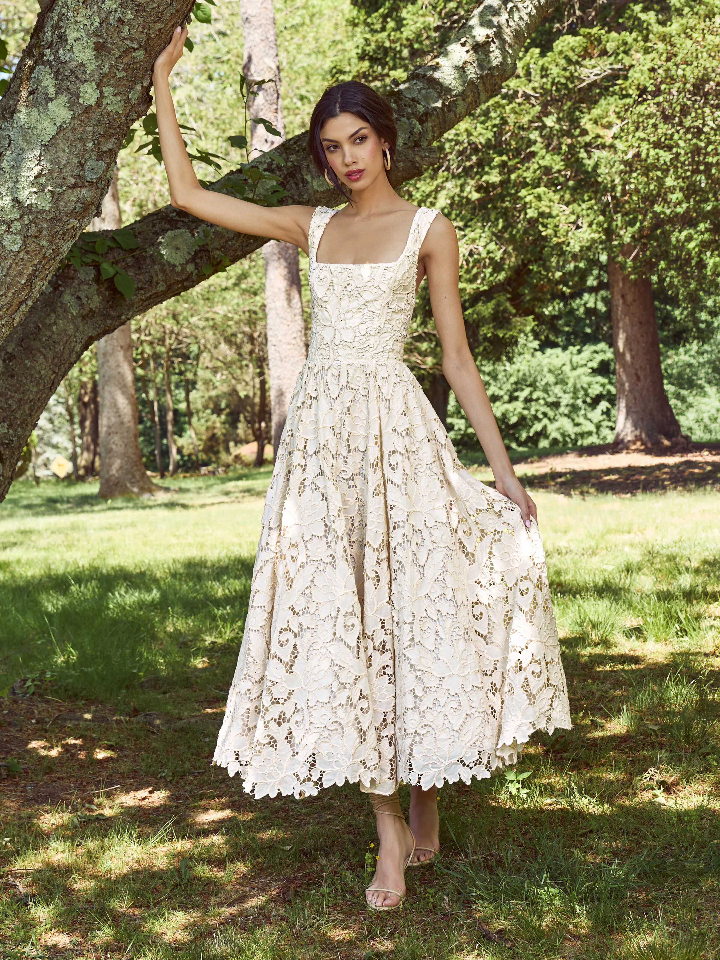 A model wearing the ALICE + OLIVIA Esma Flared Midi Dress in natural, styled with a layered look in a bright editorial setting.