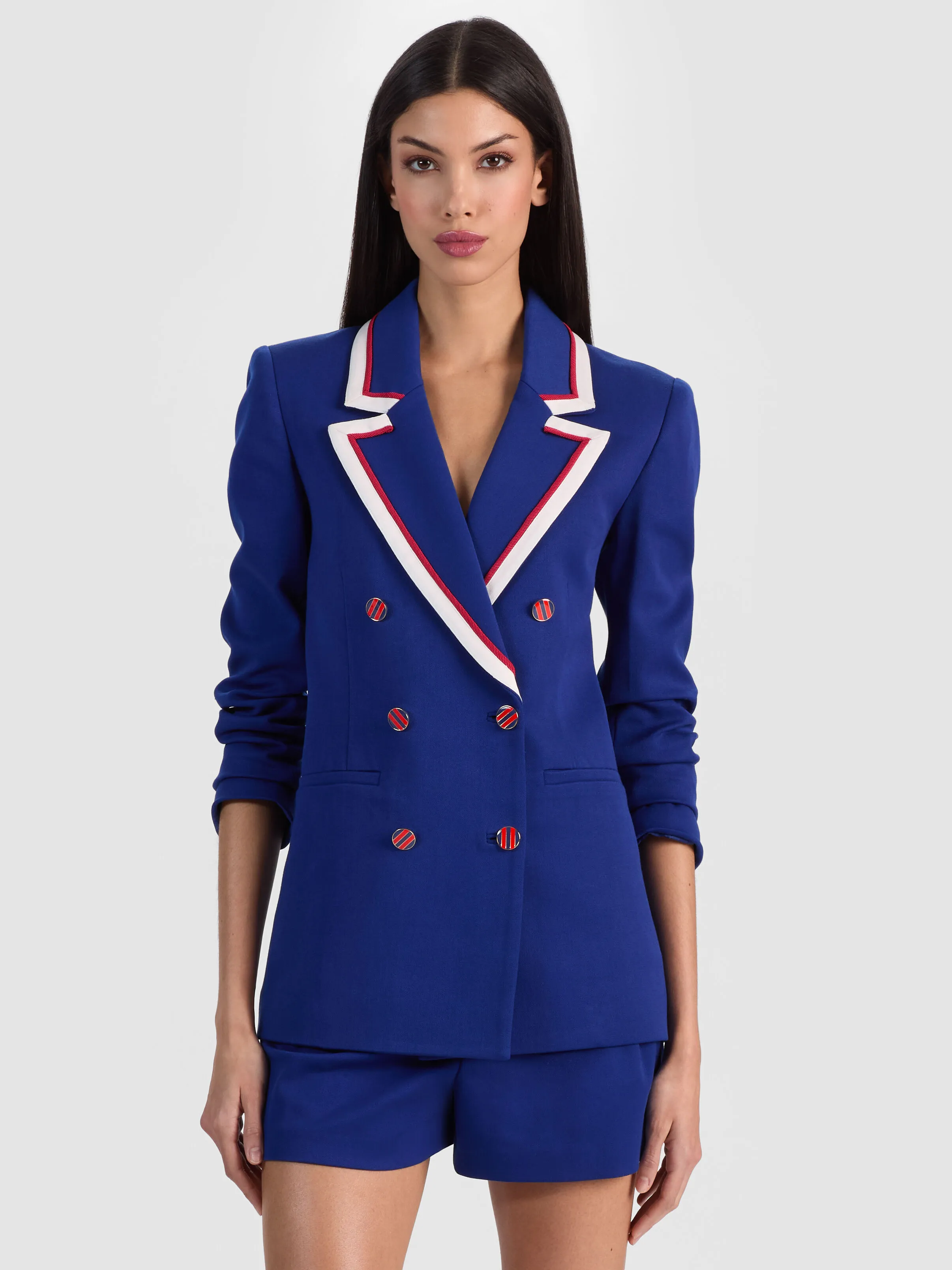 A model wearing the ALICE + OLIVIA Campbell Double Breasted Blazer in a bold blue hue with piped lapels and strong shoulders, styled as a complete suiting look.