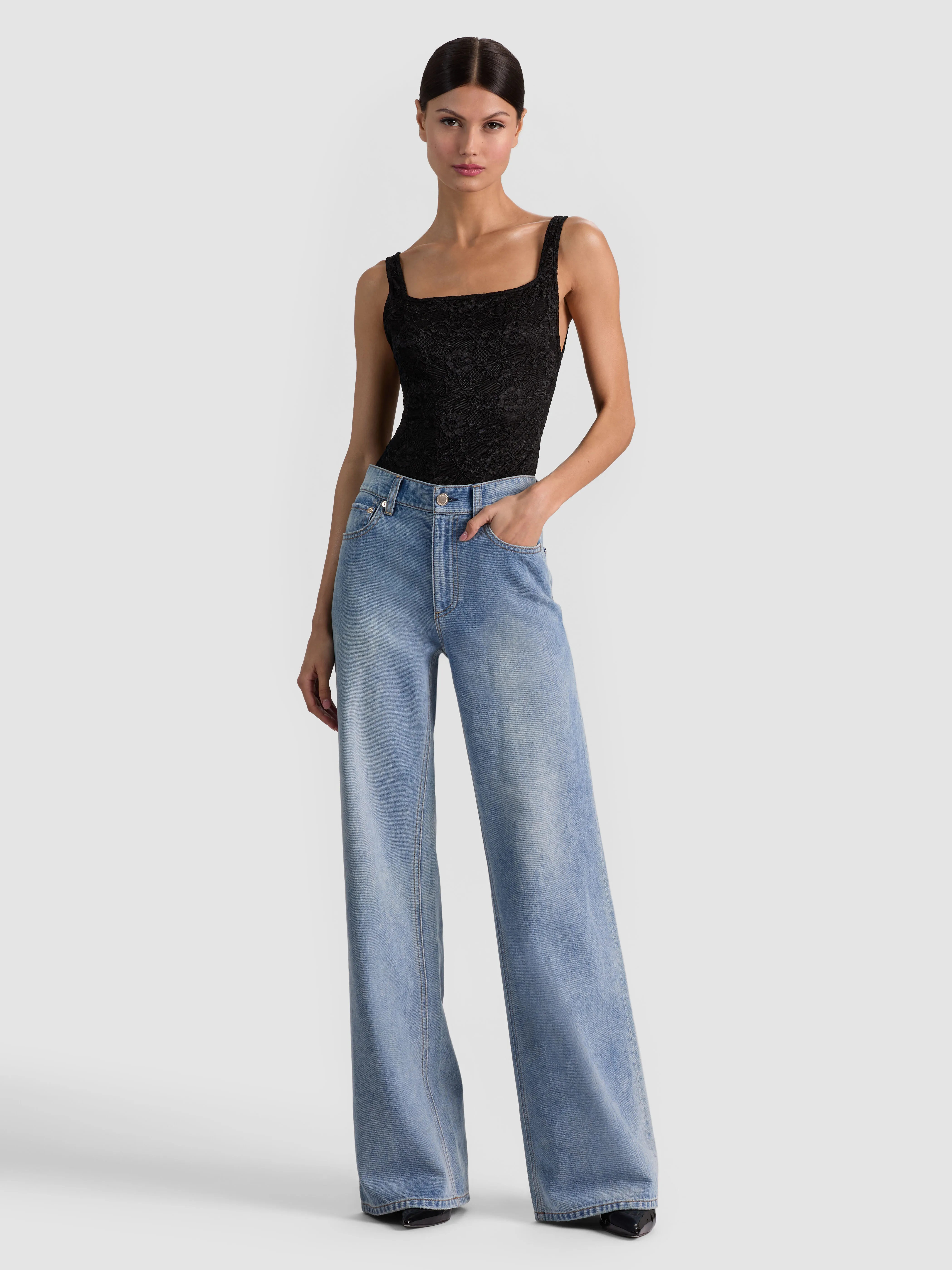 A full-body head-to-toe editorial shot of a model wearing the ALICE + OLIVIA Chic Jean in Erika Wash, showcasing the complete outfit including face, top, and full wide-leg silhouette.