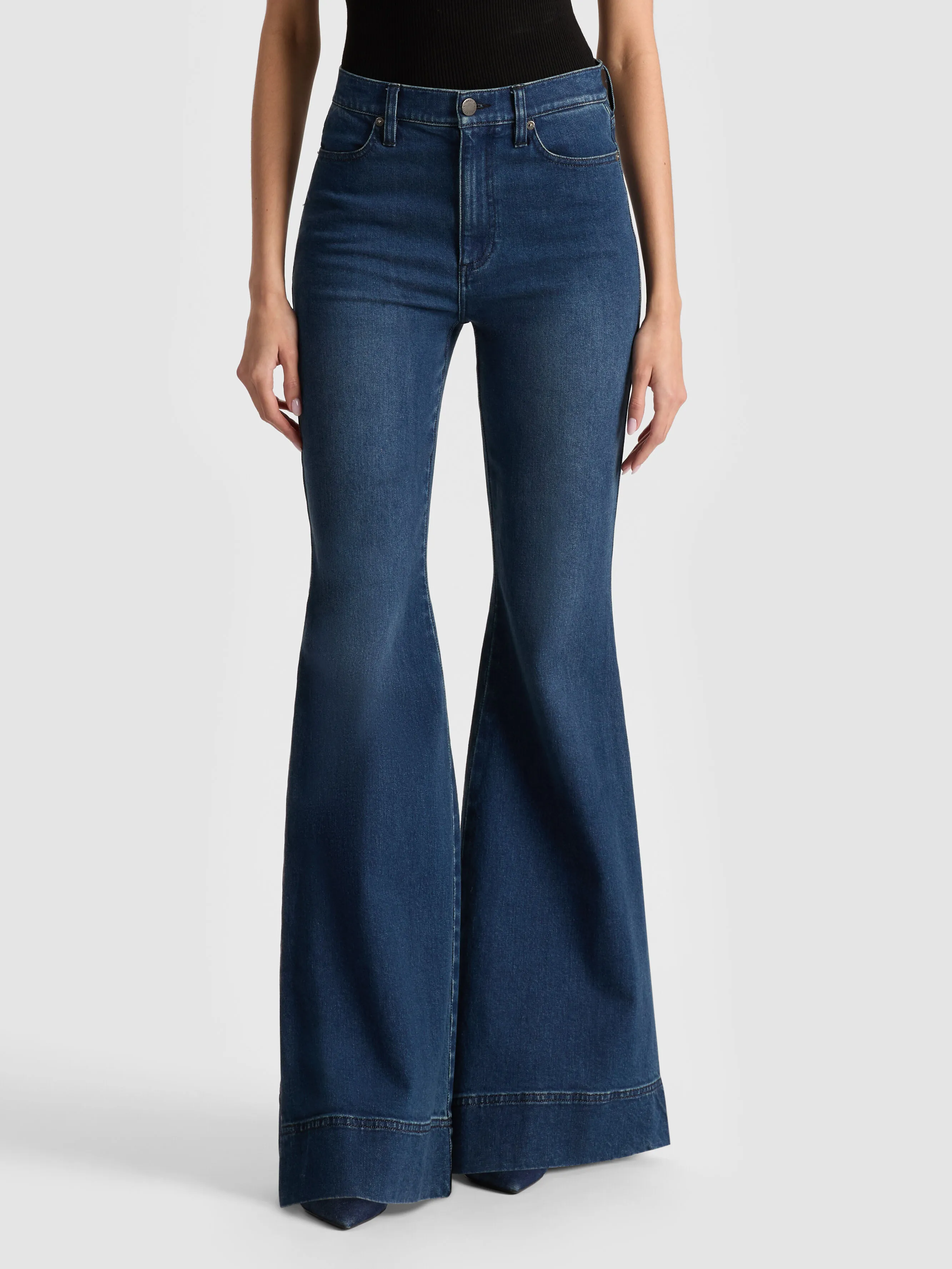 A full-length shot of a woman wearing the ALICE + OLIVIA Beautiful Jean bell-bottom style with a wide hem and dark wash, representing the 2026 bootcut and flared silhouette denim trend.