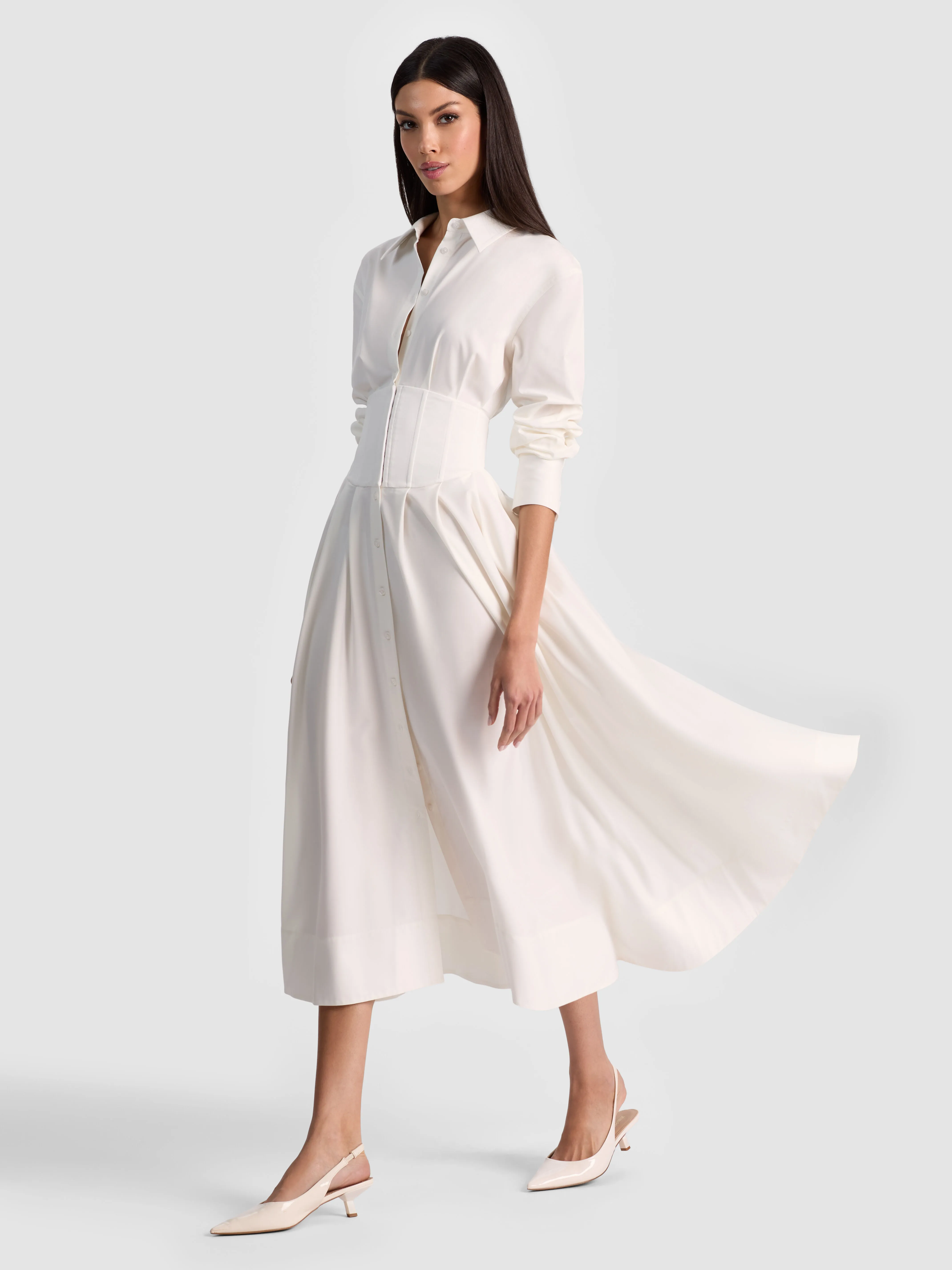 A model wearing the EDIE CORSET MIDI SHIRT DRESS in white lightweight twill with a corseted waist and button-down front, paired with loafers for a polished daytime office look.