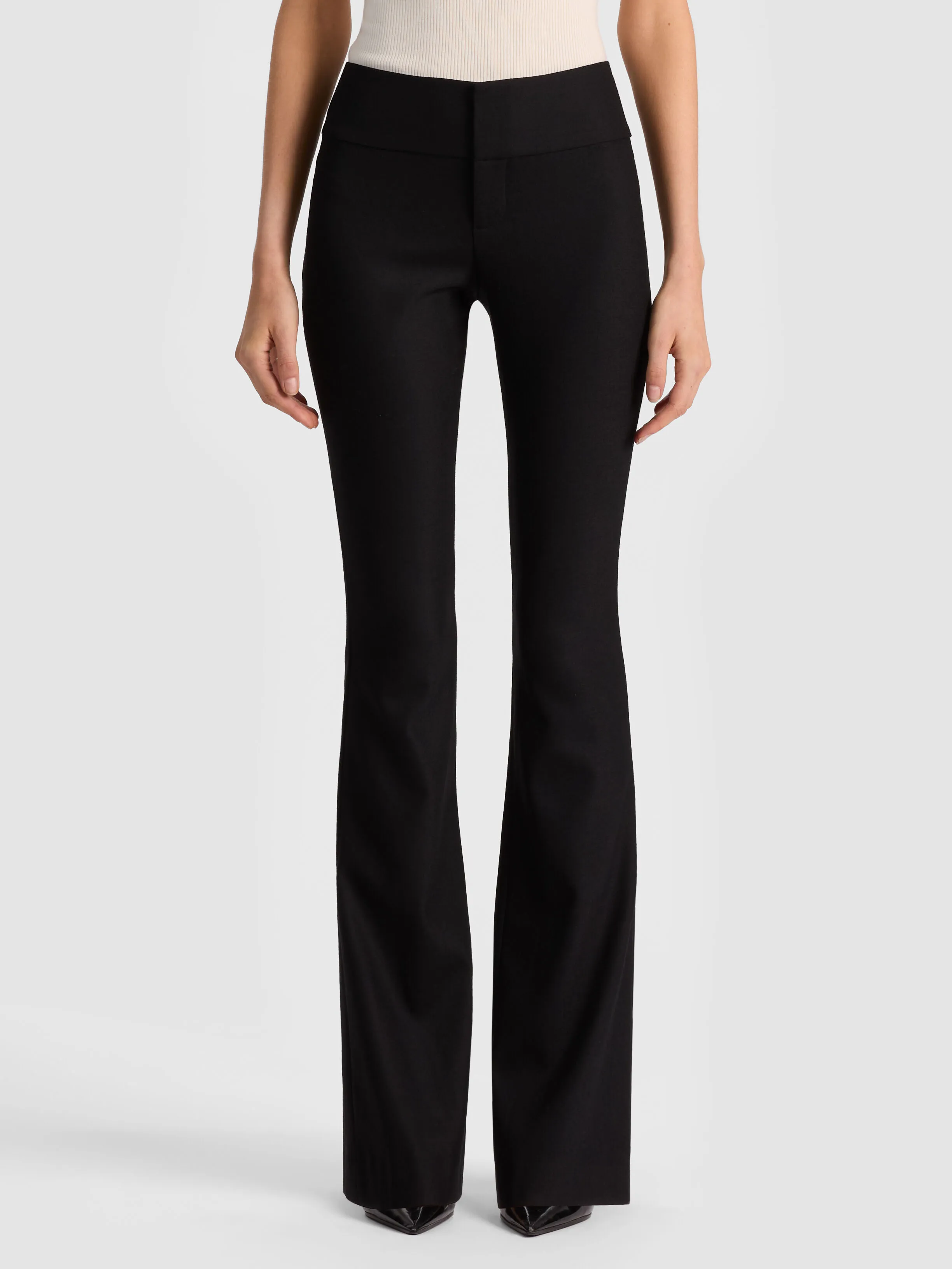 A sleek editorial shot of the ALICE + OLIVIA Olivia Wool Bootcut Pant in black wool sateen, styled with a fitted blazer for a polished suiting look in a bright, minimal studio.