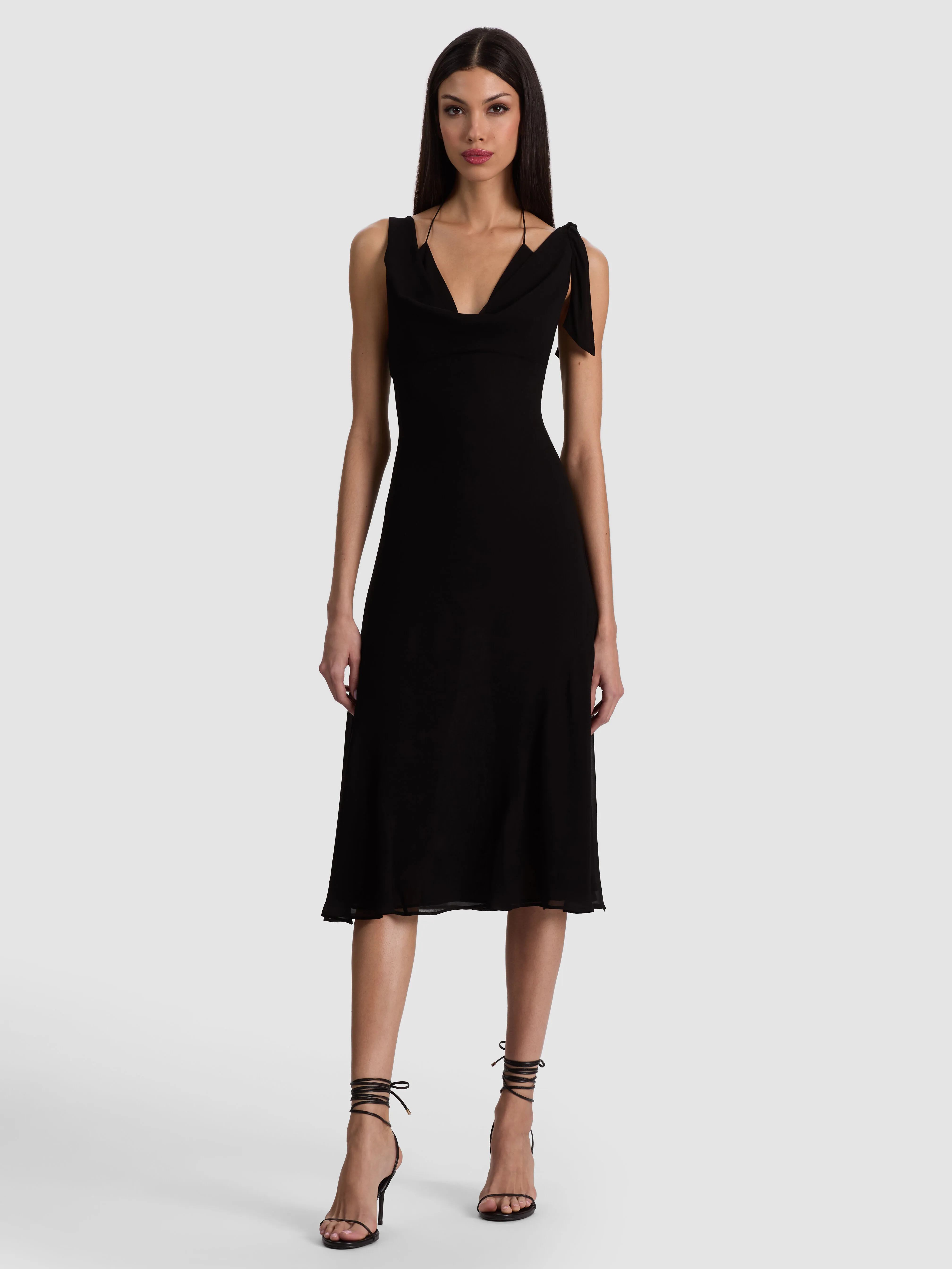 A model wearing the Abigail Bikini Midi Dress in black, styled with bold accessories including statement jewelry, polished heels, and a chic bag, photographed in an elegant setting.