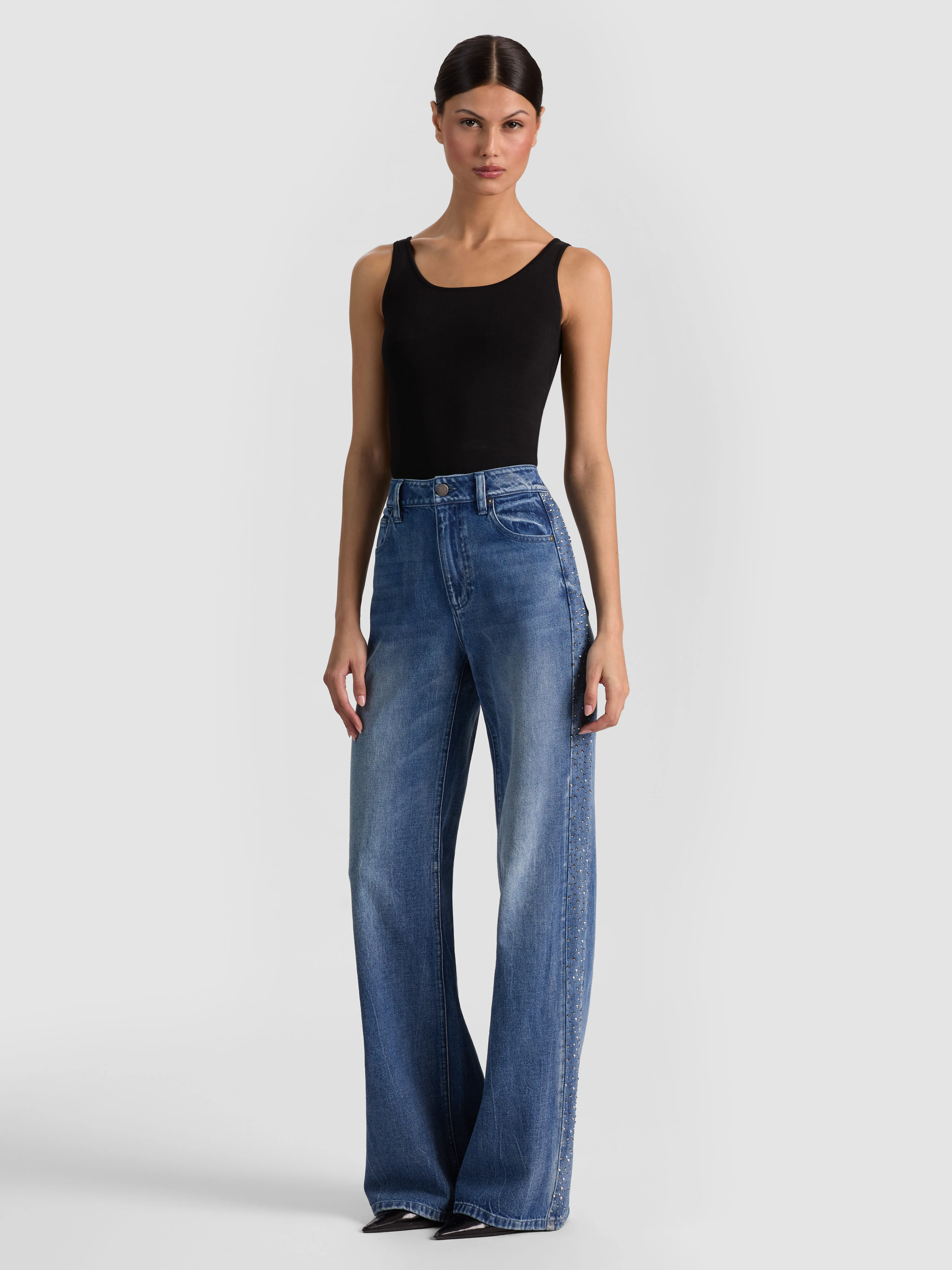 Full-body head-to-toe shot of a model wearing the ALICE + OLIVIA Chic Embellished Jean in Brooklyn Blue/Hematite, styled for a relaxed travel day with a tee, cardigan, and loafers.