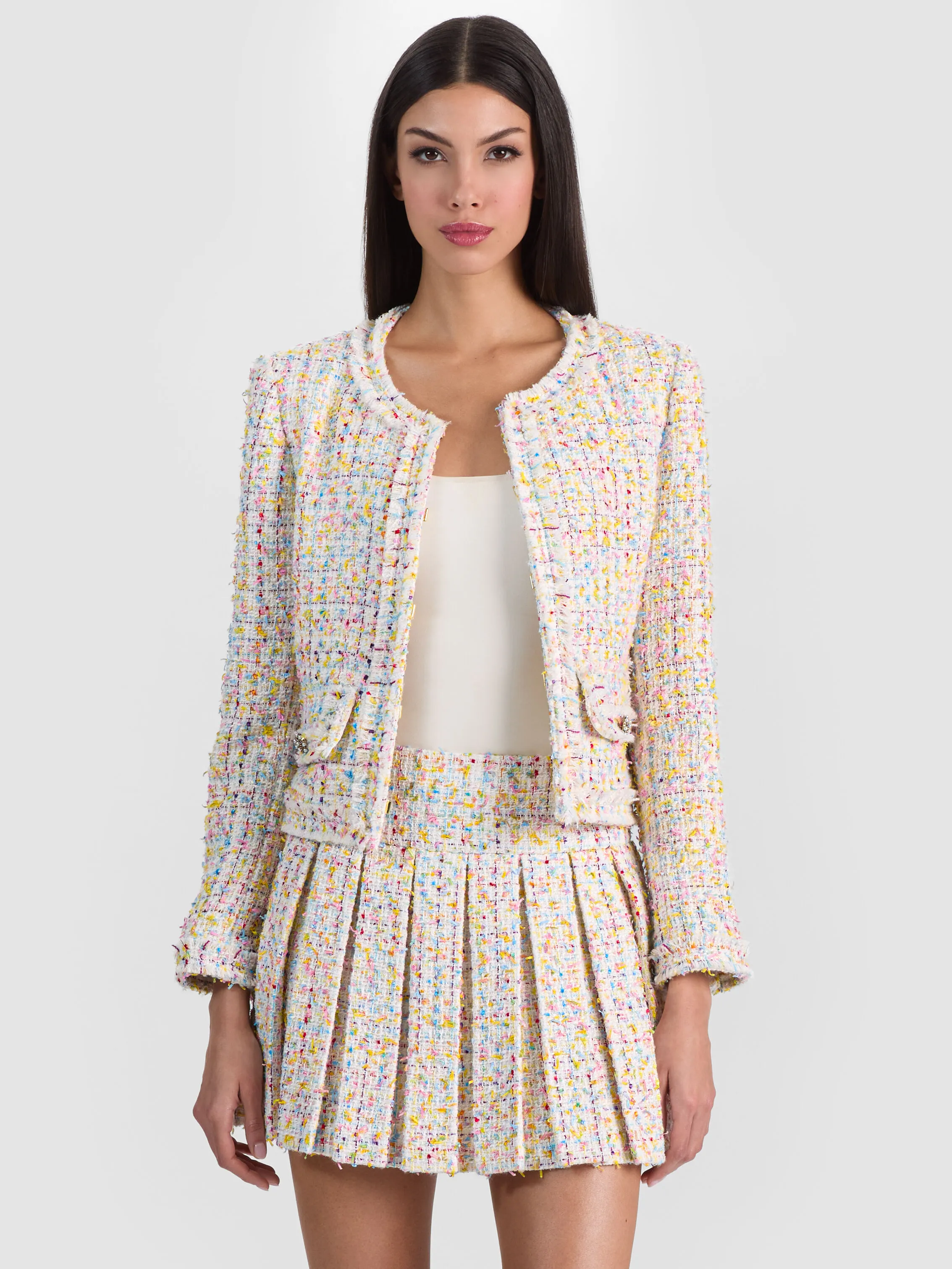 A model wearing the ALICE + OLIVIA Landon Cropped Jacket paired with the matching Emilie Tweed Mini Skirt, styled as a complete skirt suit look in rainbow eyelash boucle tweed.