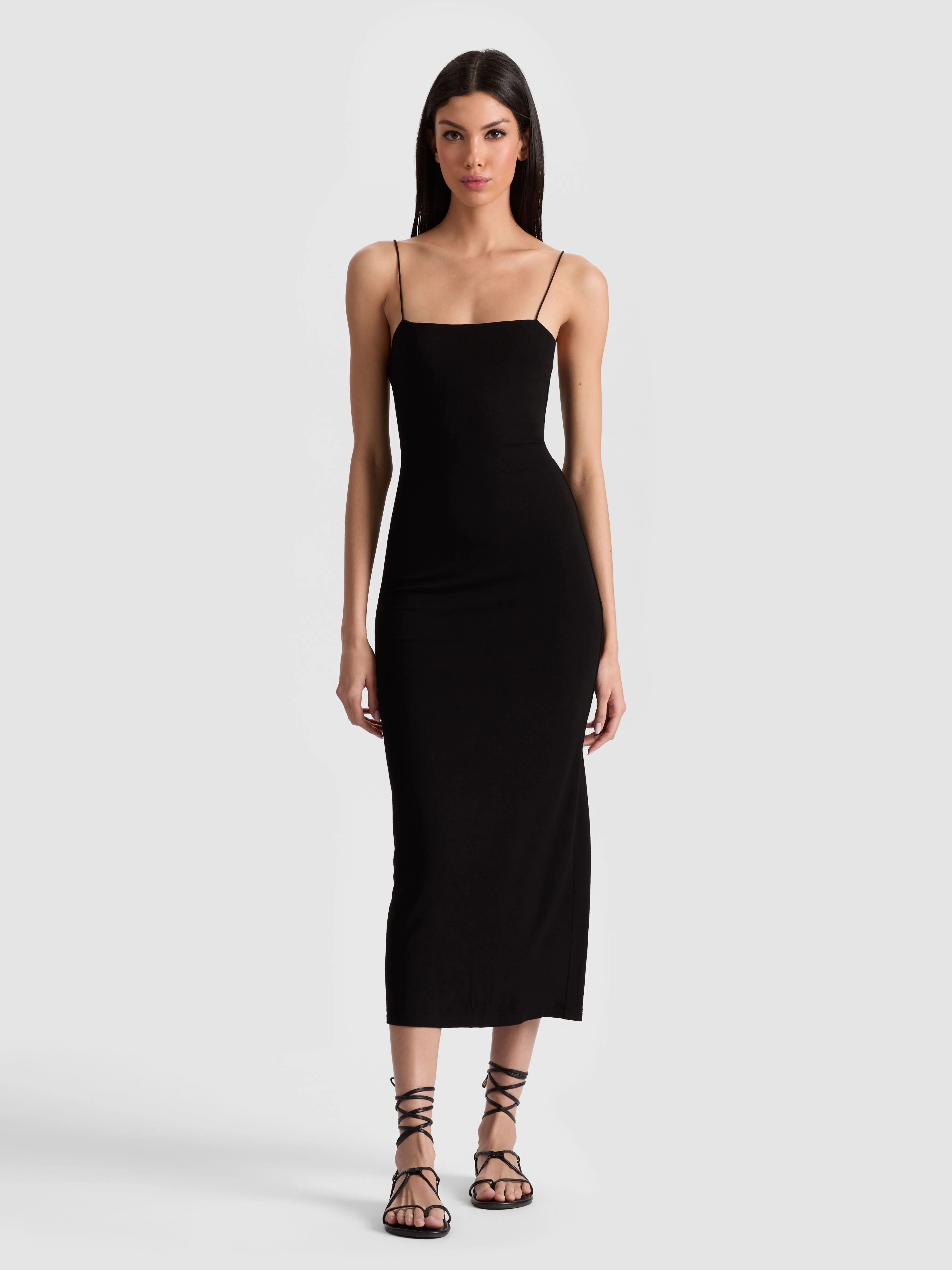 A woman wearing the FIFI MIDI DRESS — a sleek black bodycon midi with spaghetti straps and a back slit — styled with pointed-toe pumps for a sophisticated evening occasion.