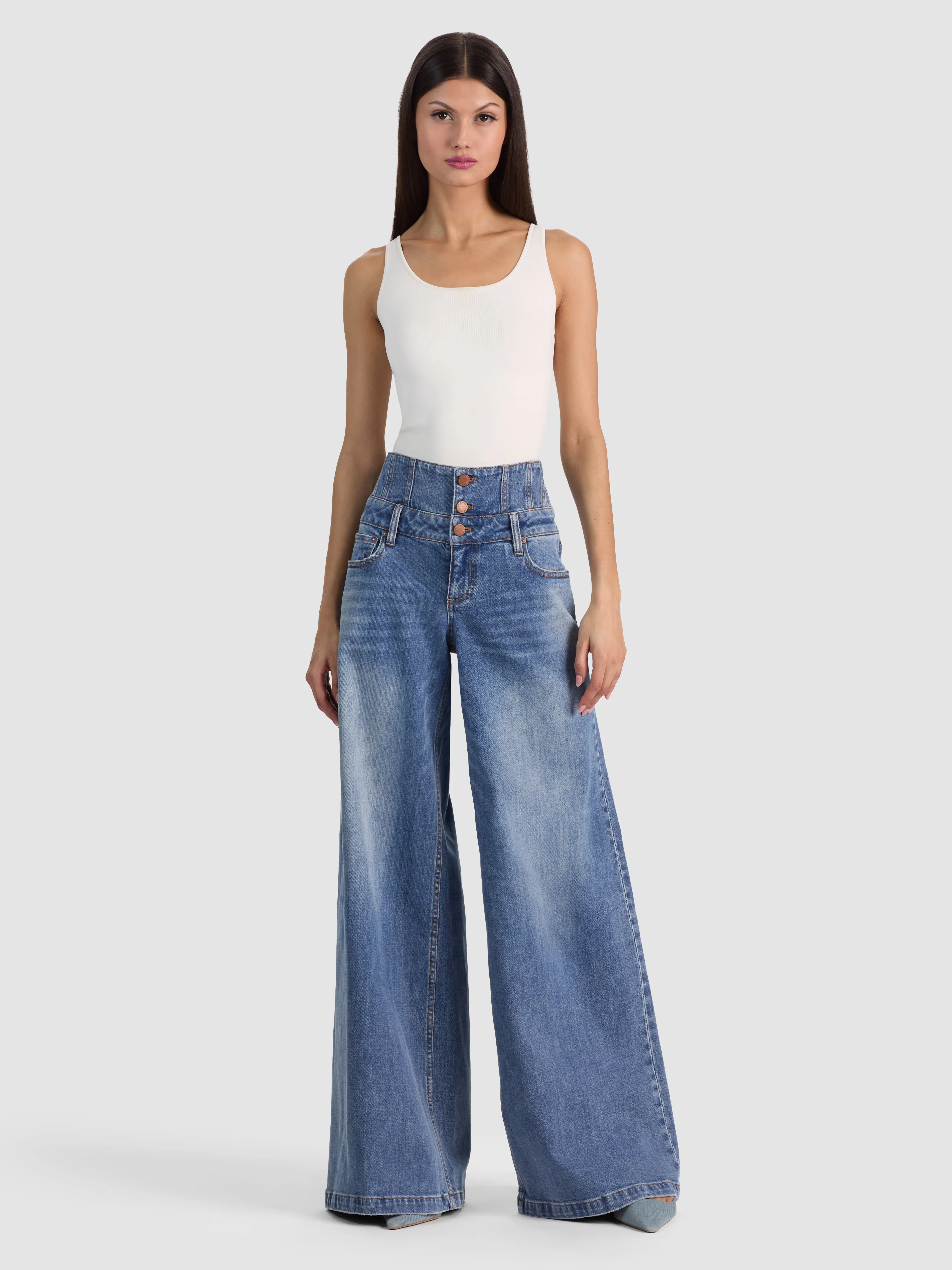 Full-body on-model shot of the ALICE + OLIVIA Whit Ultra High Button Front Jean in Brooklyn Blue, showing the complete head-to-toe look paired with a cropped knit sweater.