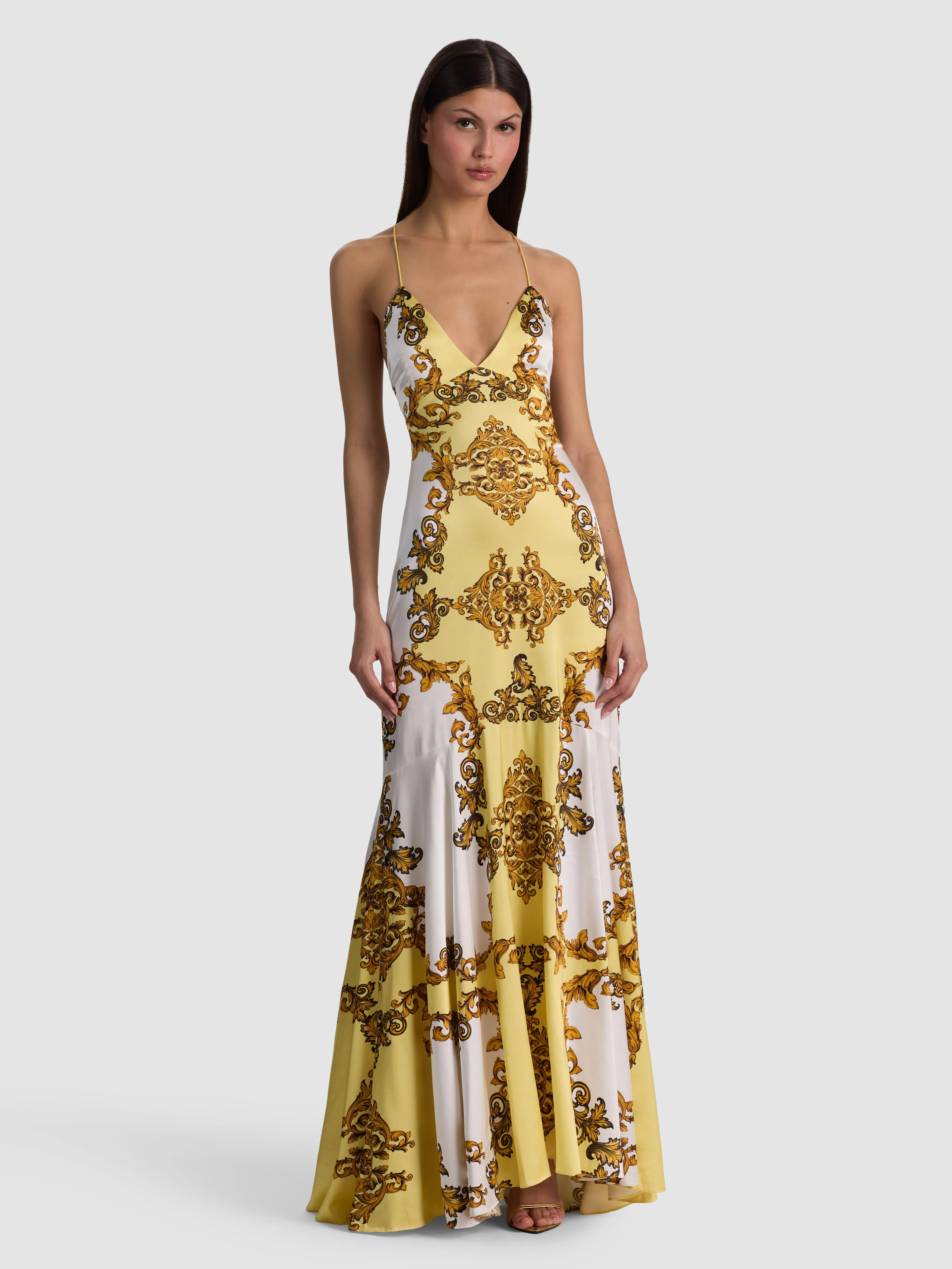 The ALICE + OLIVIA Milta Mermaid Slip Dress in Golden Coast baroque print glossy viscose satin, featuring a plunging V-neckline and open crisscross back, styled for a formal evening event.