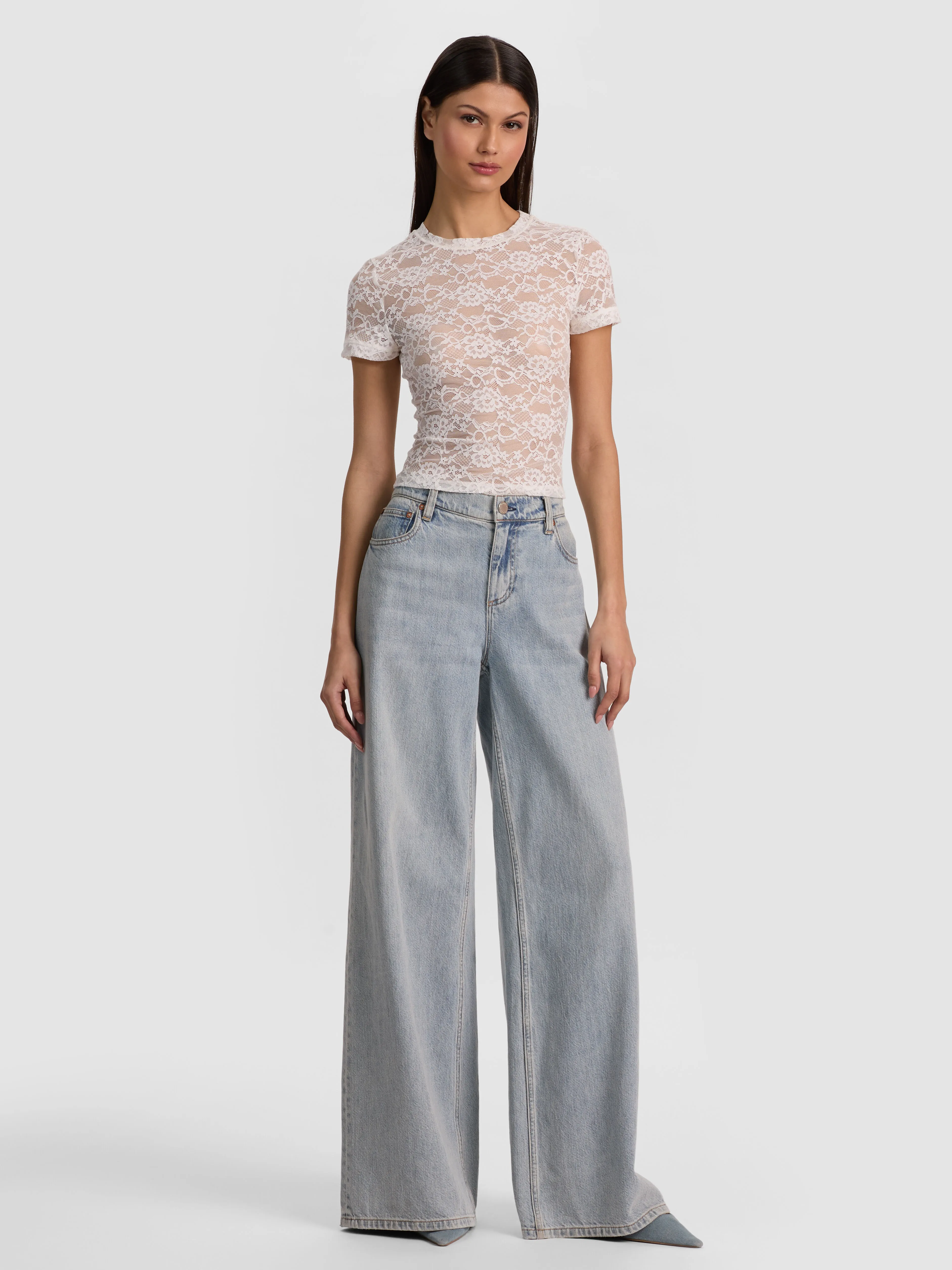 Full-body head-to-toe shot of a model wearing the ALICE + OLIVIA Amazing Jean in Darla Light Indigo, styled for a weekend casual look with a cropped sweater and sneakers.