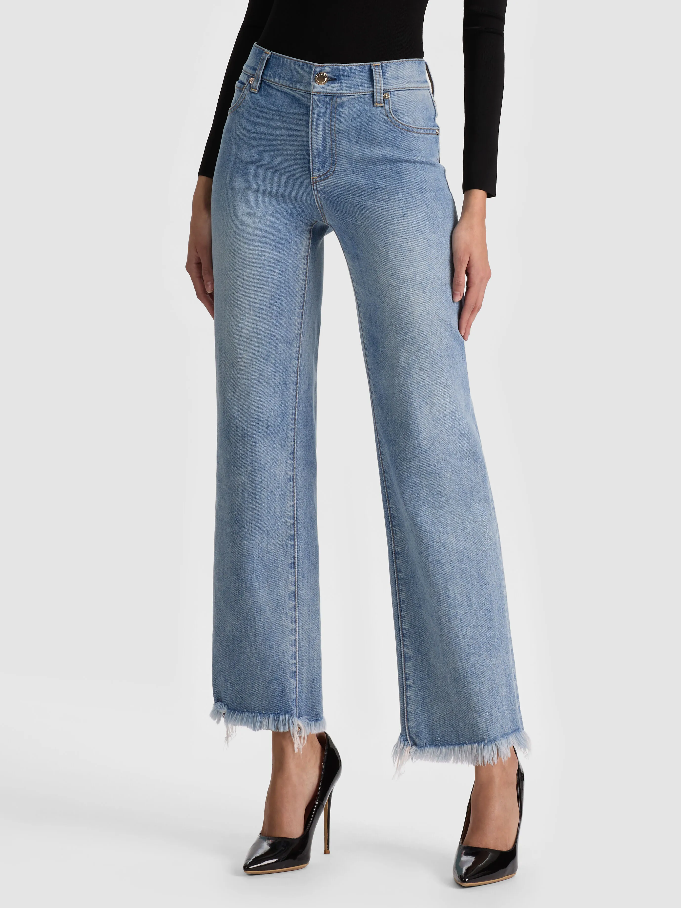 A full-length lifestyle shot of a woman wearing the ALICE + OLIVIA Fierce Jean, a classic slim straight-leg silhouette with a raw hem, styled with heeled boots, showcasing the timeless straight-leg staple denim trend for 2026.