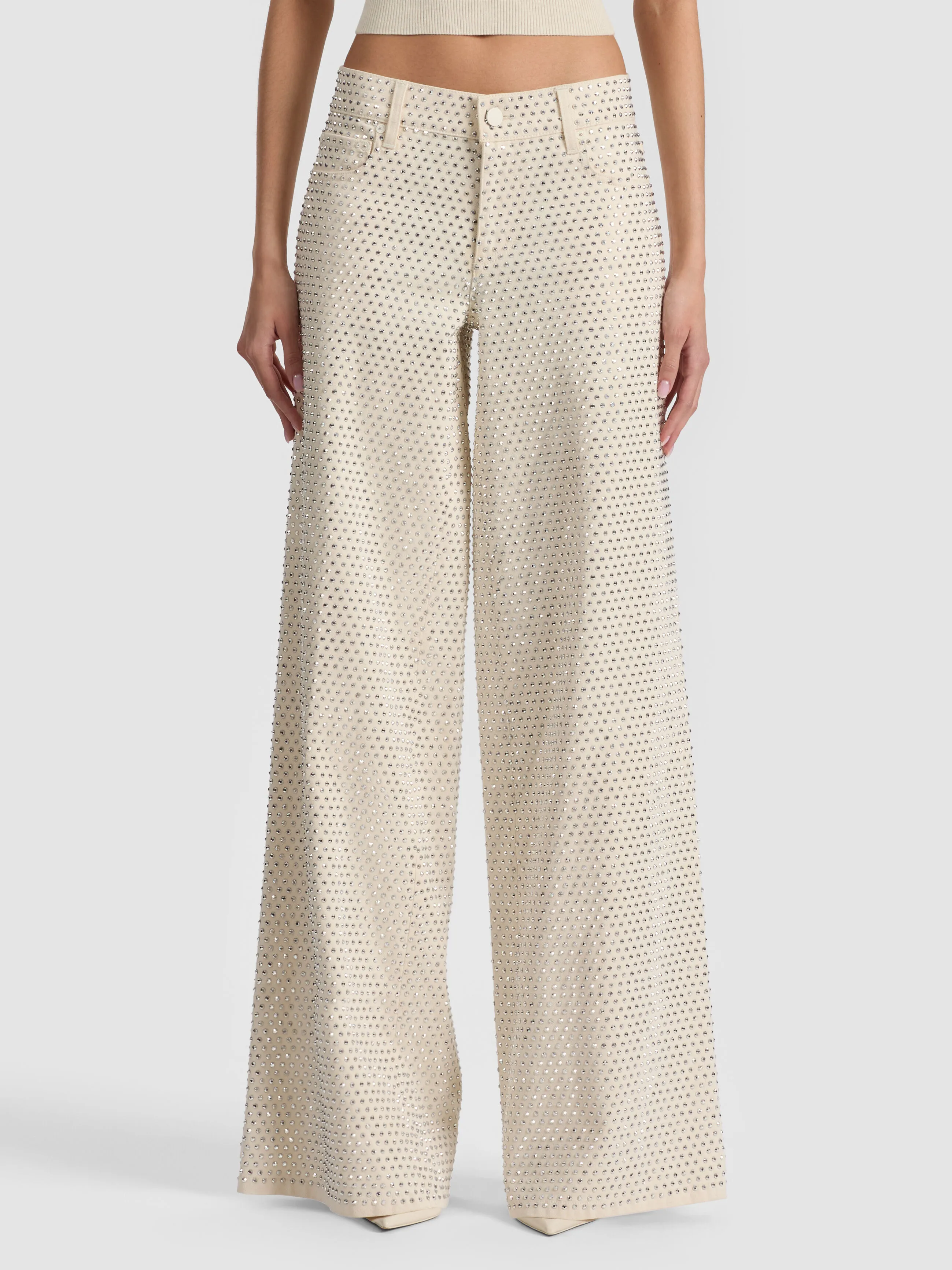 A full-length lifestyle shot of a woman wearing the ALICE + OLIVIA Amazing Embellished Jean in a wide-leg silhouette, styled with a fitted top, showcasing the relaxed yet structured 2026 wide-leg denim trend.