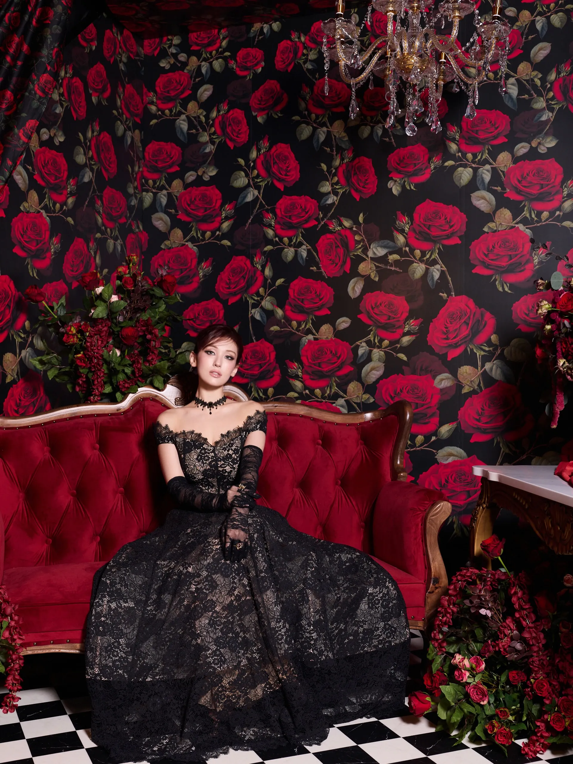 A lifestyle shot of models at a glamorous event wearing a red textured gown and a black butterfly-print dress, holding a turquoise retro telephone, in a gold-trimmed luxurious setting.