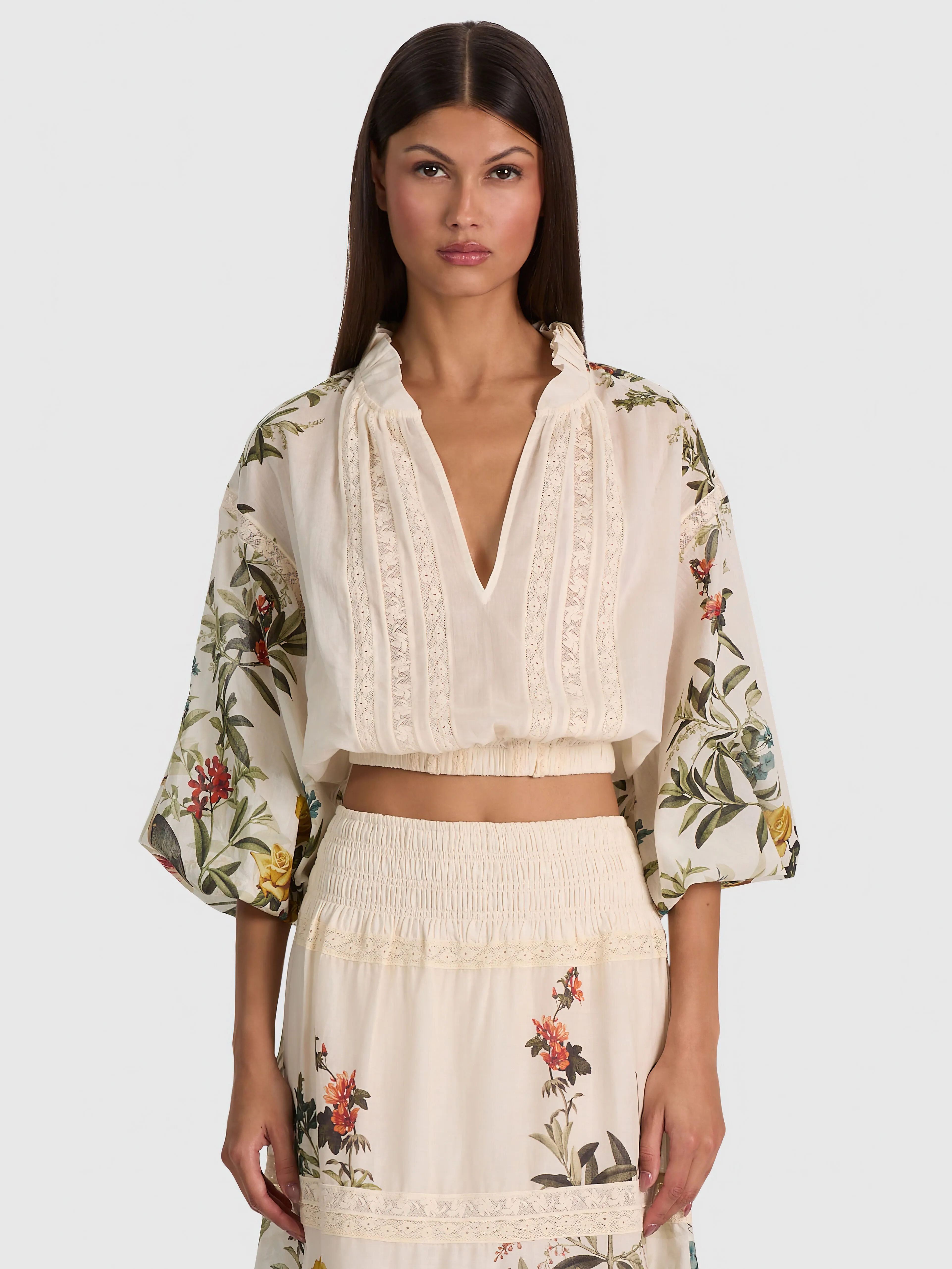 A model in the CASSIE EMBROIDERED BLOUSE and STEVIE MAXI SKIRT in Desert Sprigs Vanilla, standing in a sunlit garden, the tiered skirt flowing in the breeze.