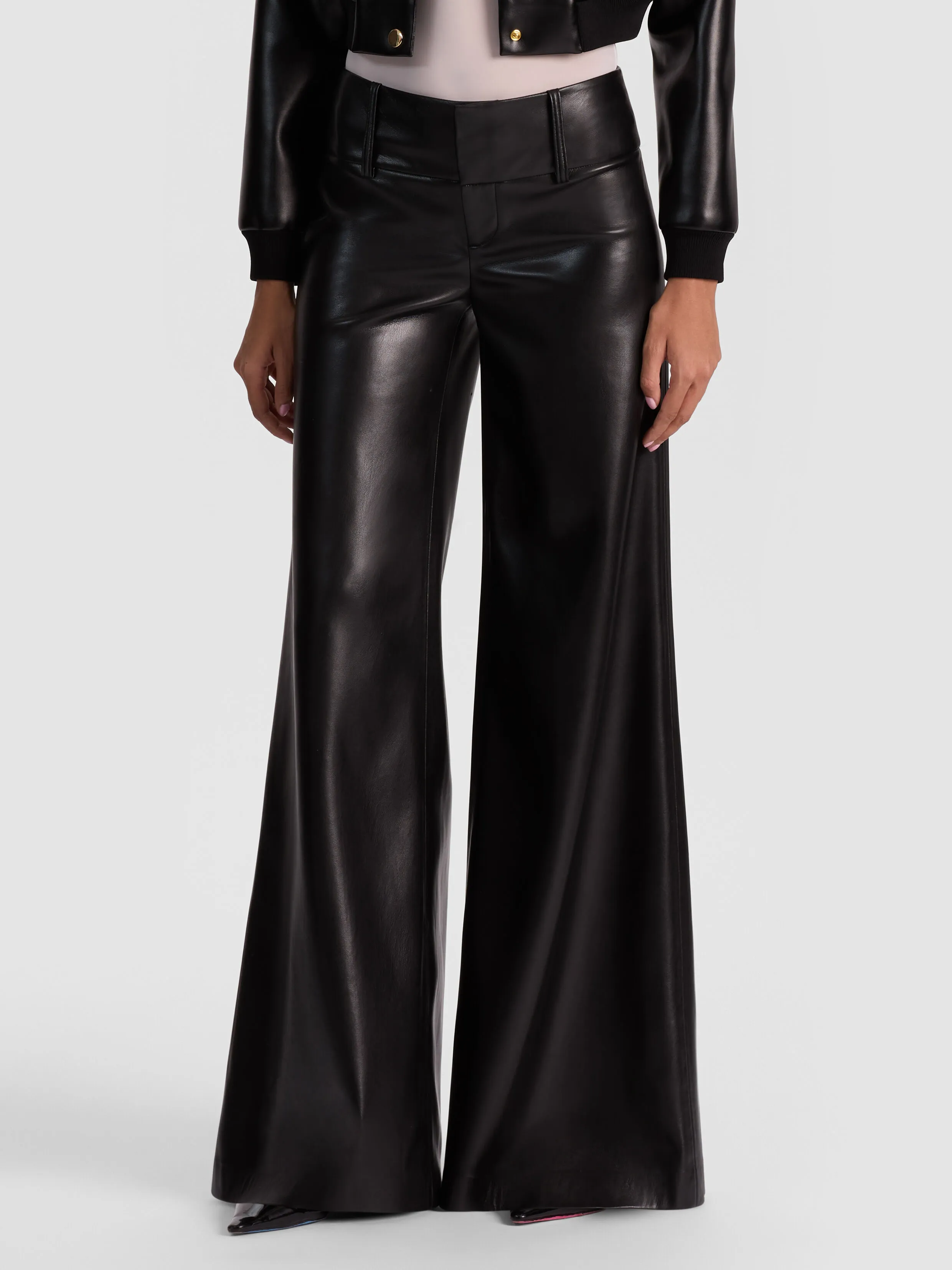 A full-length editorial shot of the ALICE + OLIVIA Olivia Vegan Wide Leg Pant in black, styled with a silk blouse and heels, against a sleek studio backdrop.