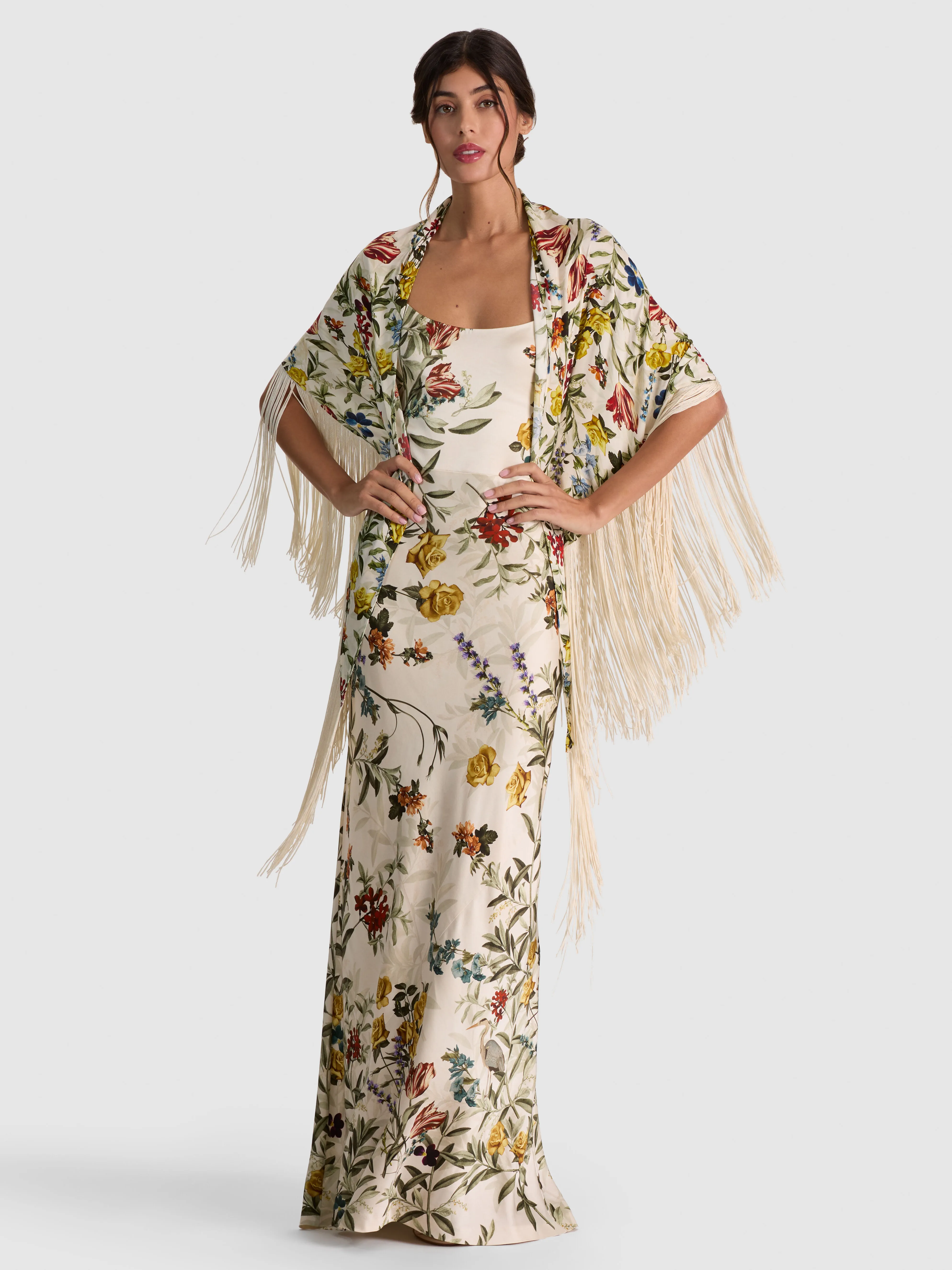 A model wearing the ALICE + OLIVIA Mesha Shawl in Desert Sprigs Vanilla, a printed satin shawl with fringe trim draped elegantly over the shoulders over an evening dress.