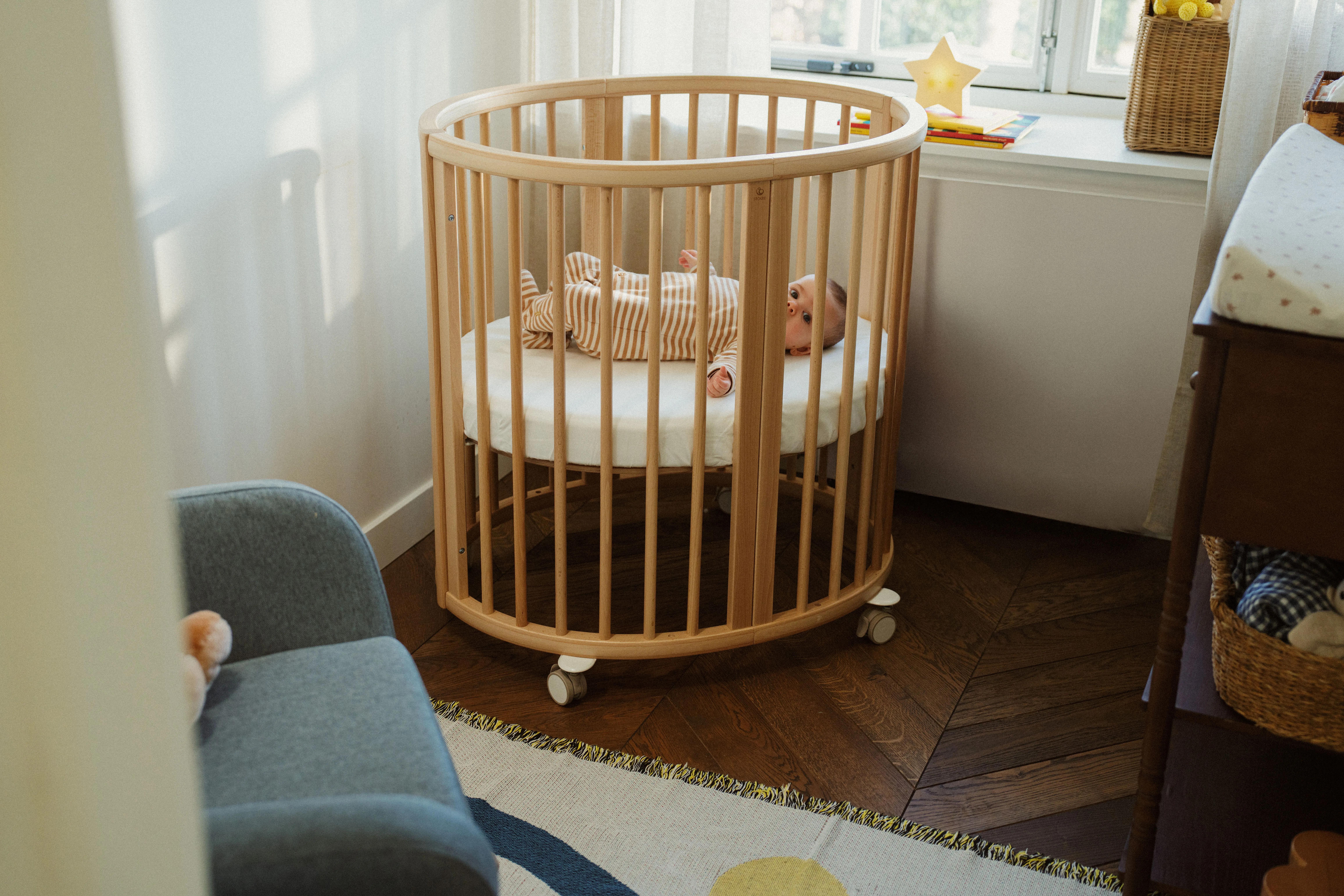 Stokke Nighti™ Convertible Cot Bed in a softly lit, beautifully styled small nursery with natural wood tones, soft neutral colours and minimal clutter, conveying calm and practicality.
