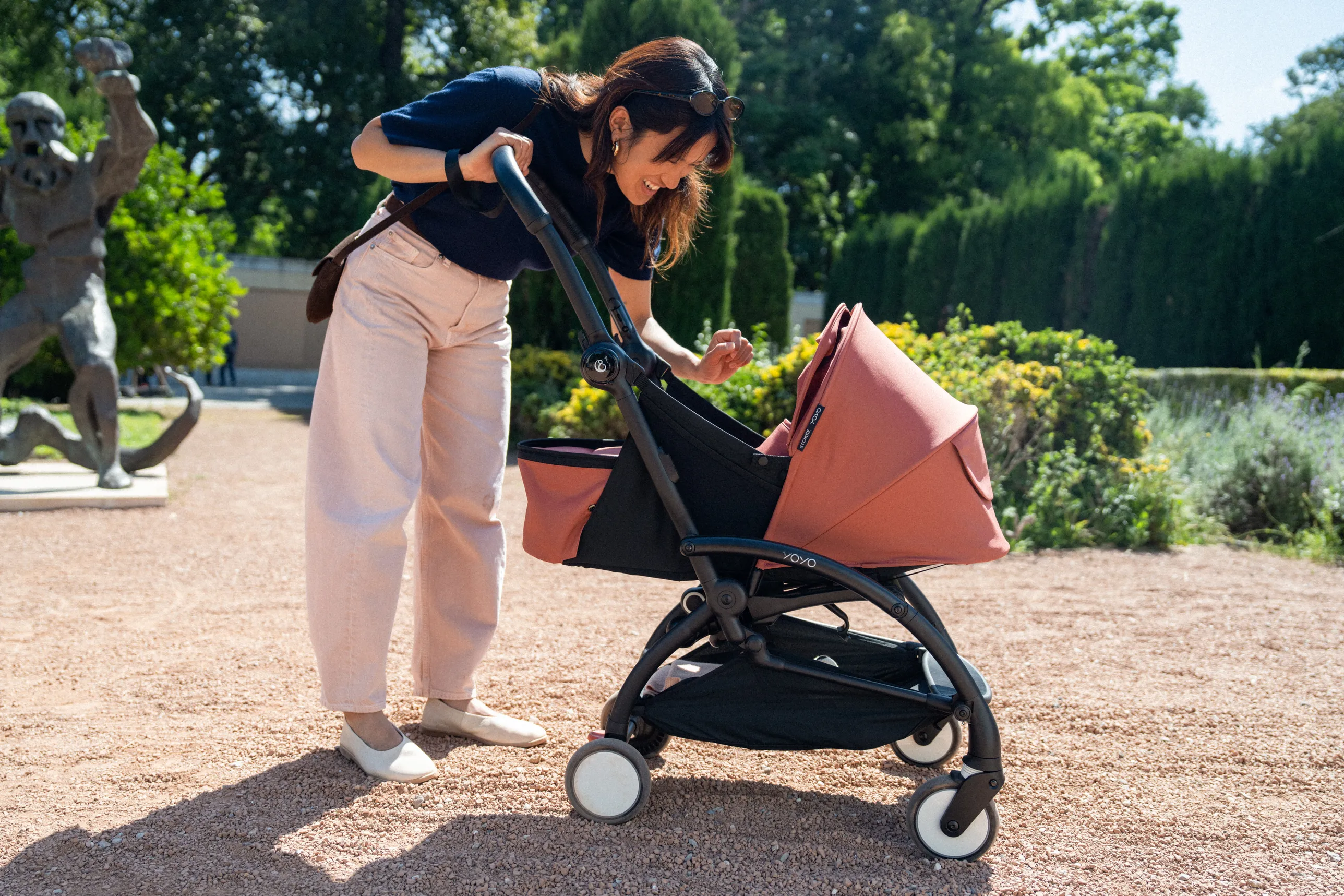 A lifestyle shot of a parent pushing a lightweight black YOYO⁵ compact stroller on a cobblestone city street in warm natural daylight.